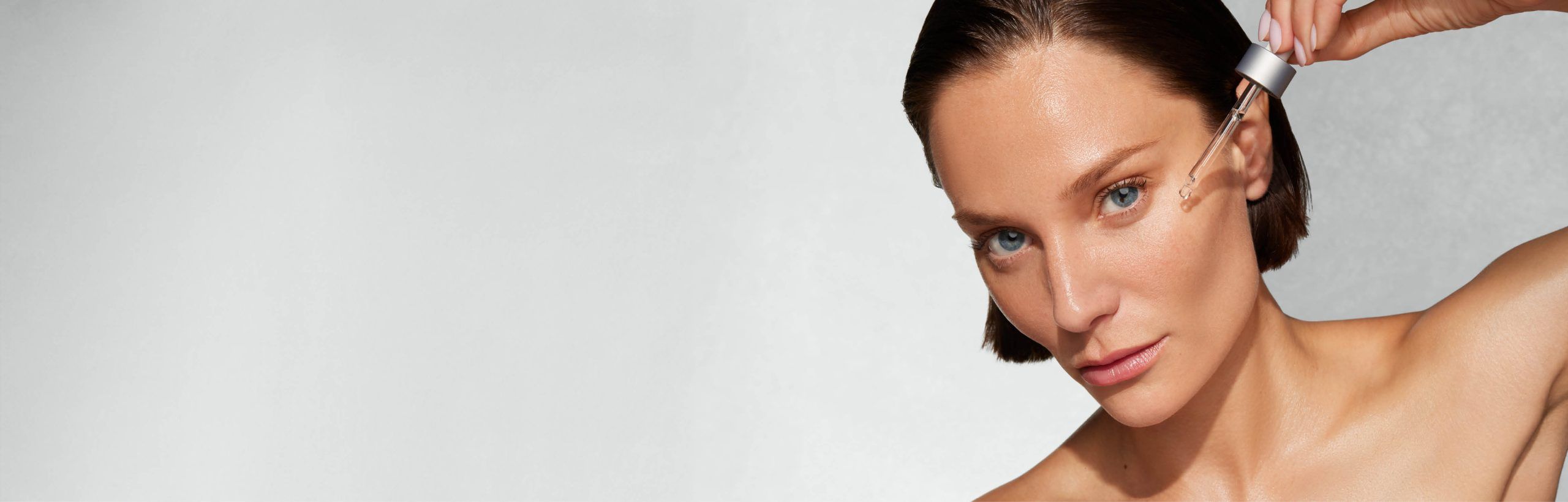 Frau mit erhobenem Arm trägt per Pipette Serum aufs Gesicht.